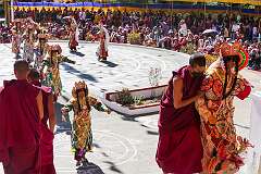 Dancers with their headdresses return up the steps to the main hall of the monastery, each accompanied by a monk.