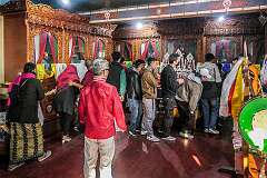 Devotees in the room with the images of the three protecting gods, in niches behind curtains that are now partly opened.