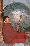 A novice monk beating a large drum at the “puja” religious ceremony.