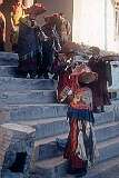 Monks in ritual robes on the steps at the start of a ceremony in Hemis Gompa; playing the Gyaling and a boy blowing on a conch shell.