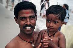 A father carrying his small son on the beach in Rameswaram.