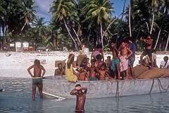 The dinghy carrying bags of copra, with local boys on top of it, off the beach in Taribo.